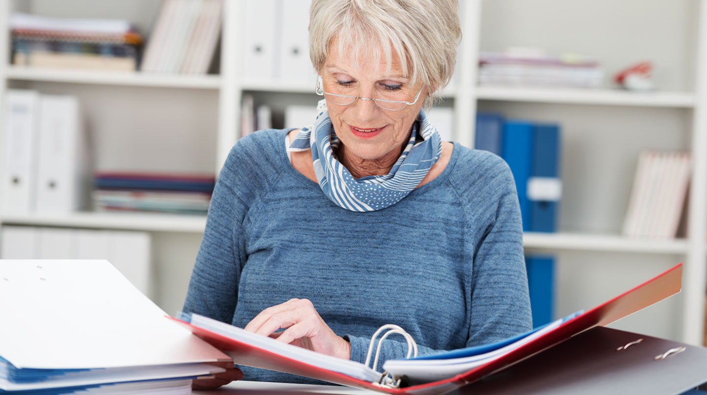 Une personne rassemble et classe méthodiquement des documents administratifs anciens, bulletins de salaire et contrats, pour une reconstitution de carrière en vue de la retraite